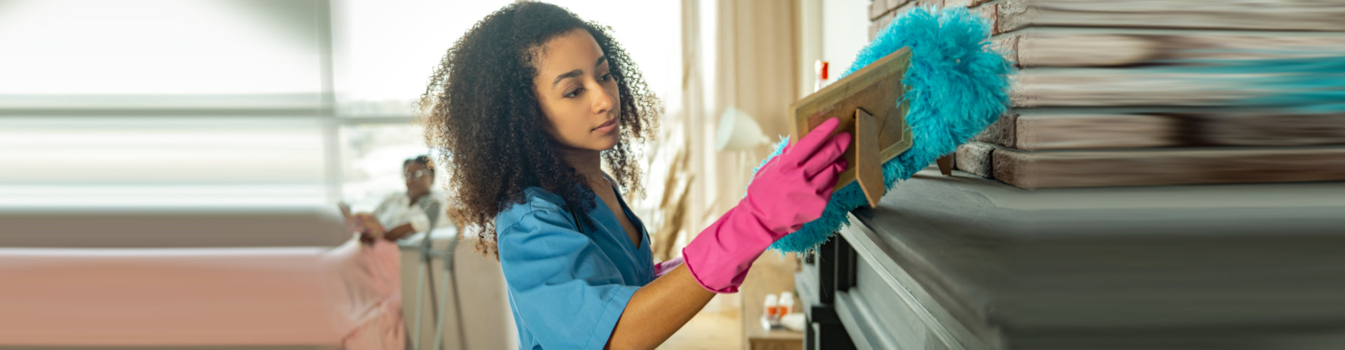 young nurse cleaning the apartment from dust while helping her patient
