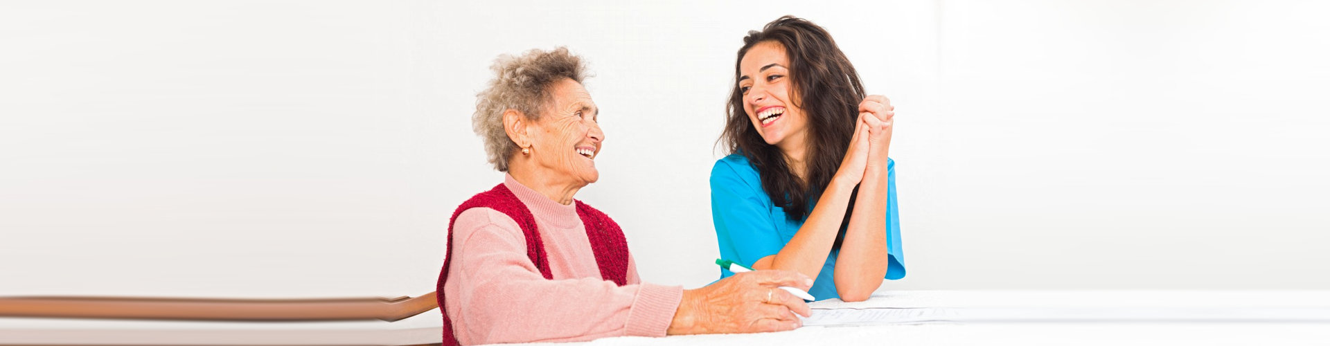 Happy elderly lady laughing with kind nurse carer working in homecare.
